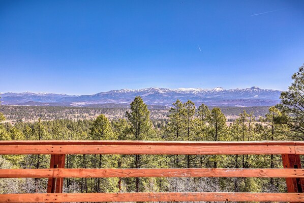 A wooden fence with a view of snow-capped mountains and a forested valley.