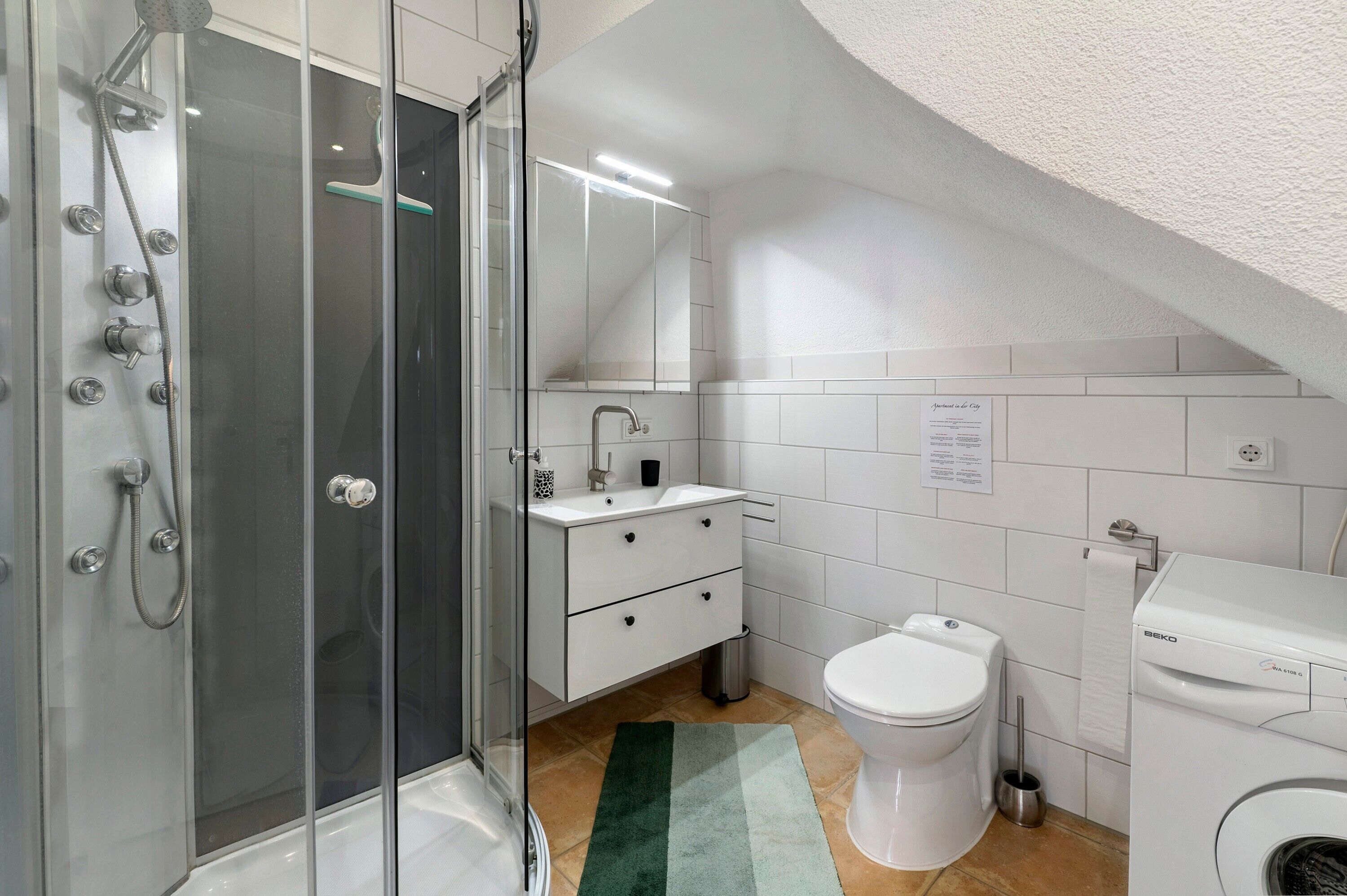 Une salle de bain moderne avec une douche à parois de verre, un lavabo blanc, des toilettes et un lave-linge.