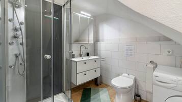 Une salle de bain moderne avec une douche à parois de verre, un lavabo blanc, des toilettes et un lave-linge.