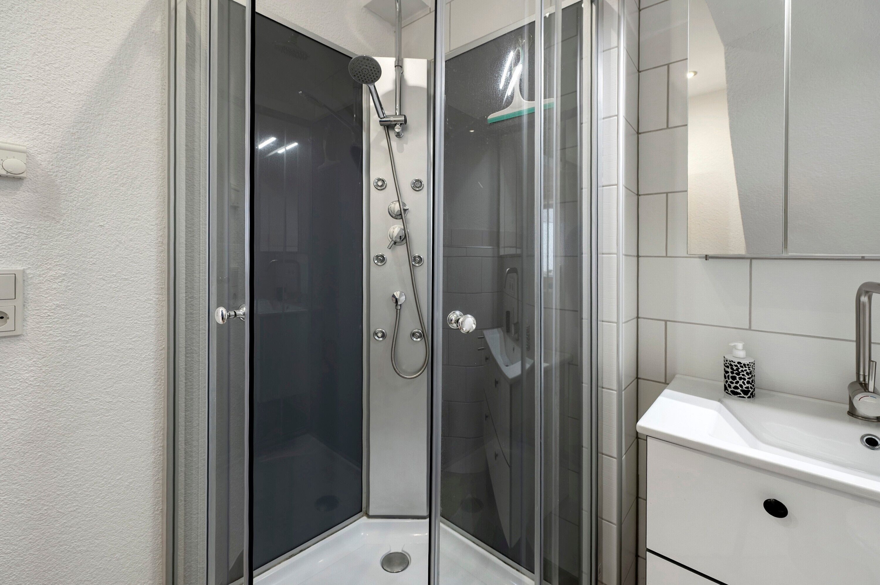 A modern bathroom with a glass-enclosed shower, a white sink, and a mirror.