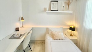 A minimalist hotel room with a white desk, a bed with white bedding, a small shelf with a framed menu, and a nightstand with a lamp. - Cozy Penthouse in the center. Air conditioning (Jerez de la frontera)