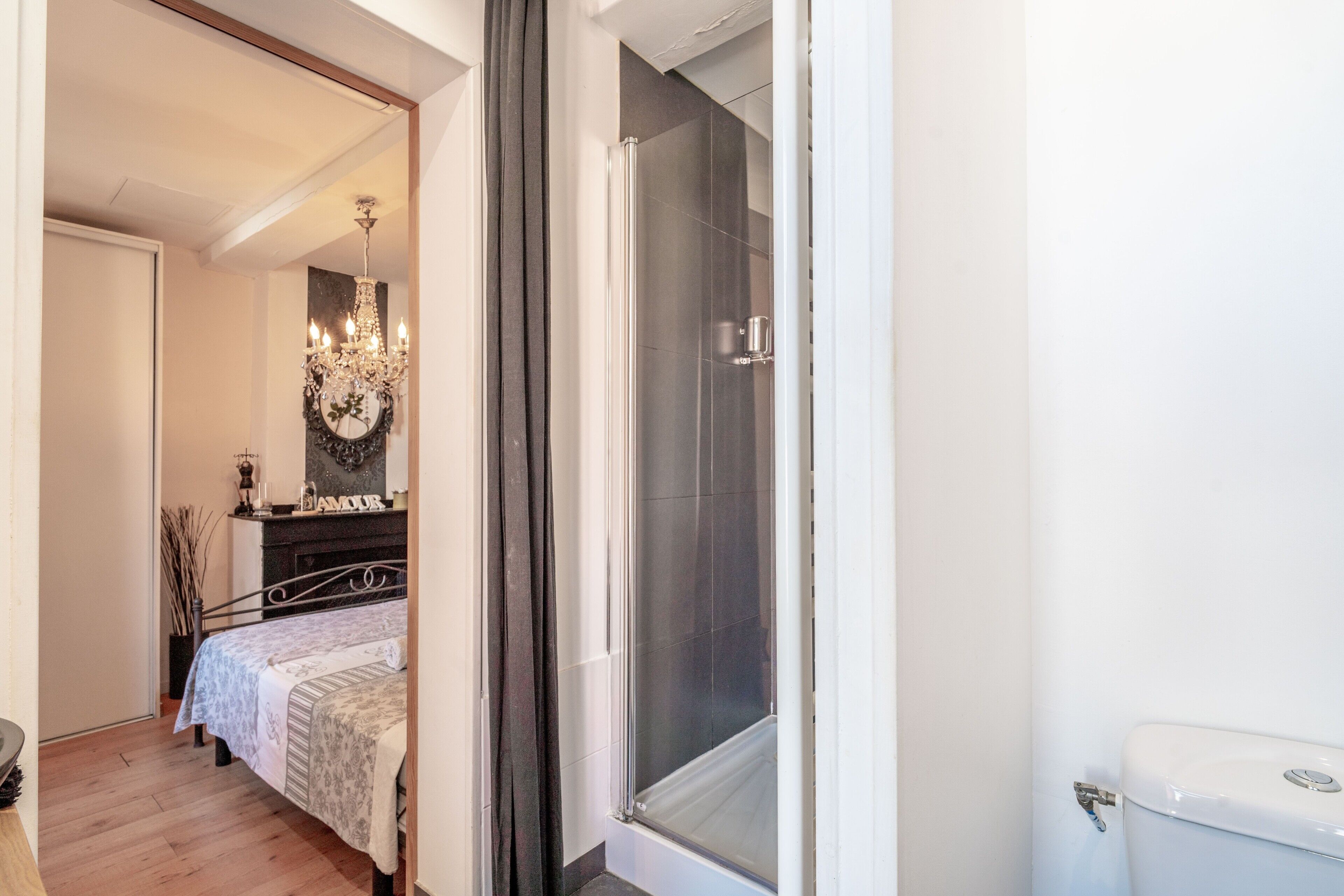 Un dormitorio con cama, cómoda, espejo, candelabro y zona de ducha.