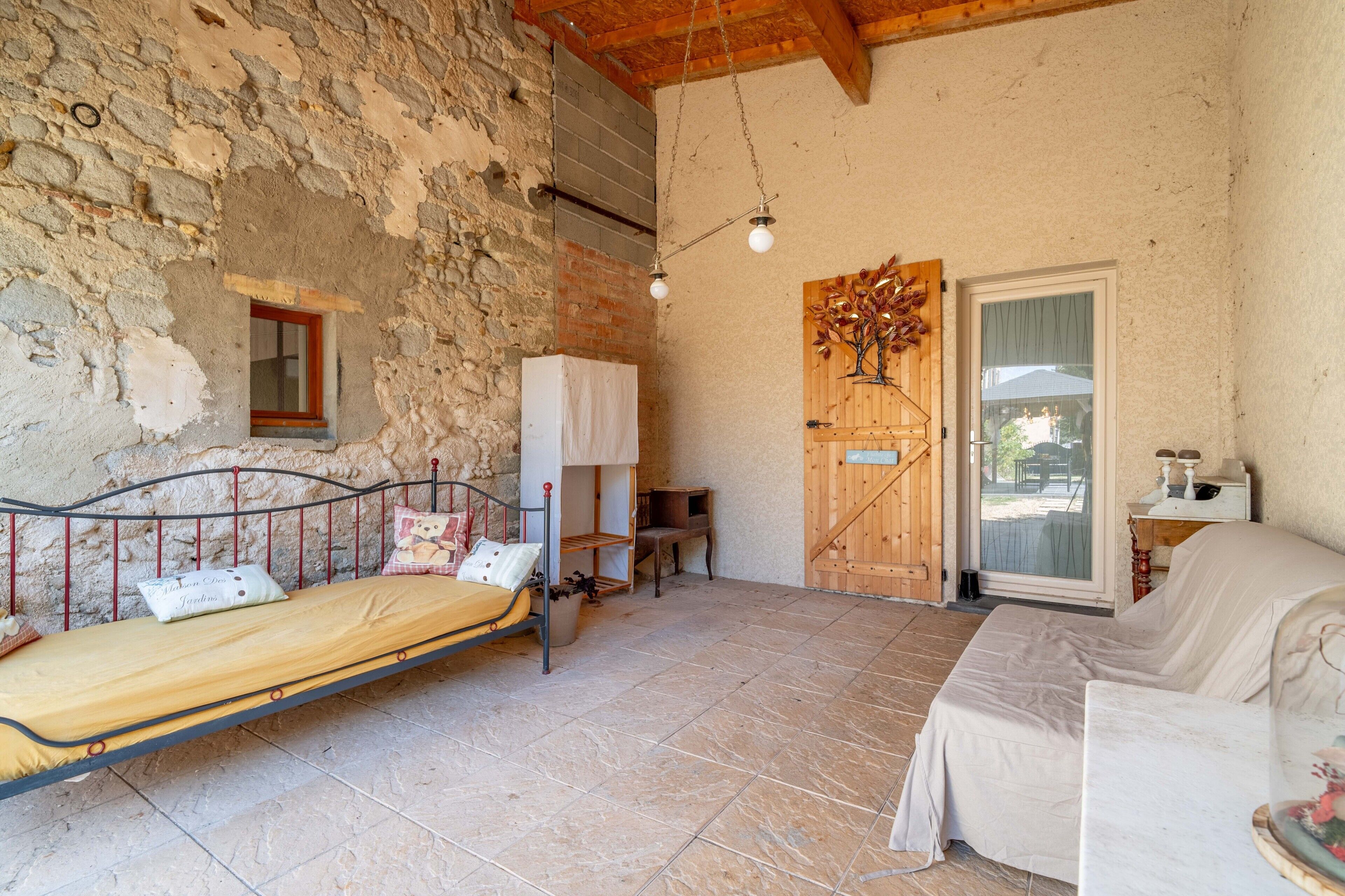 A rustic room with a bed, a wooden door, a small window, and a tiled floor.