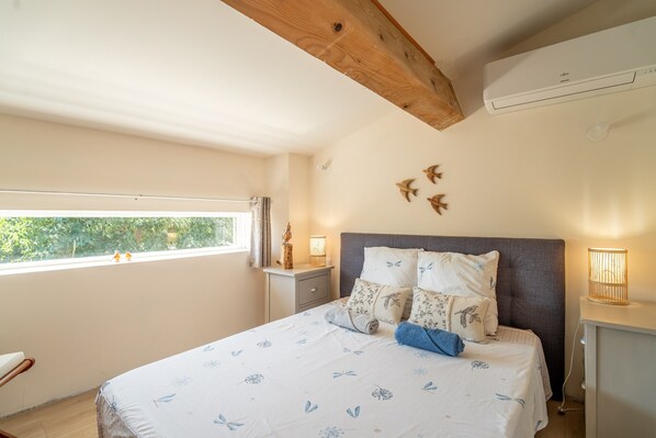 Un dormitorio con cama, mesitas de noche, una ventana y una viga en el techo.