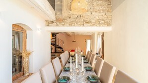 Un comedor con una mesa larga dispuesta para seis personas, paredes de piedra y una escalera al fondo.