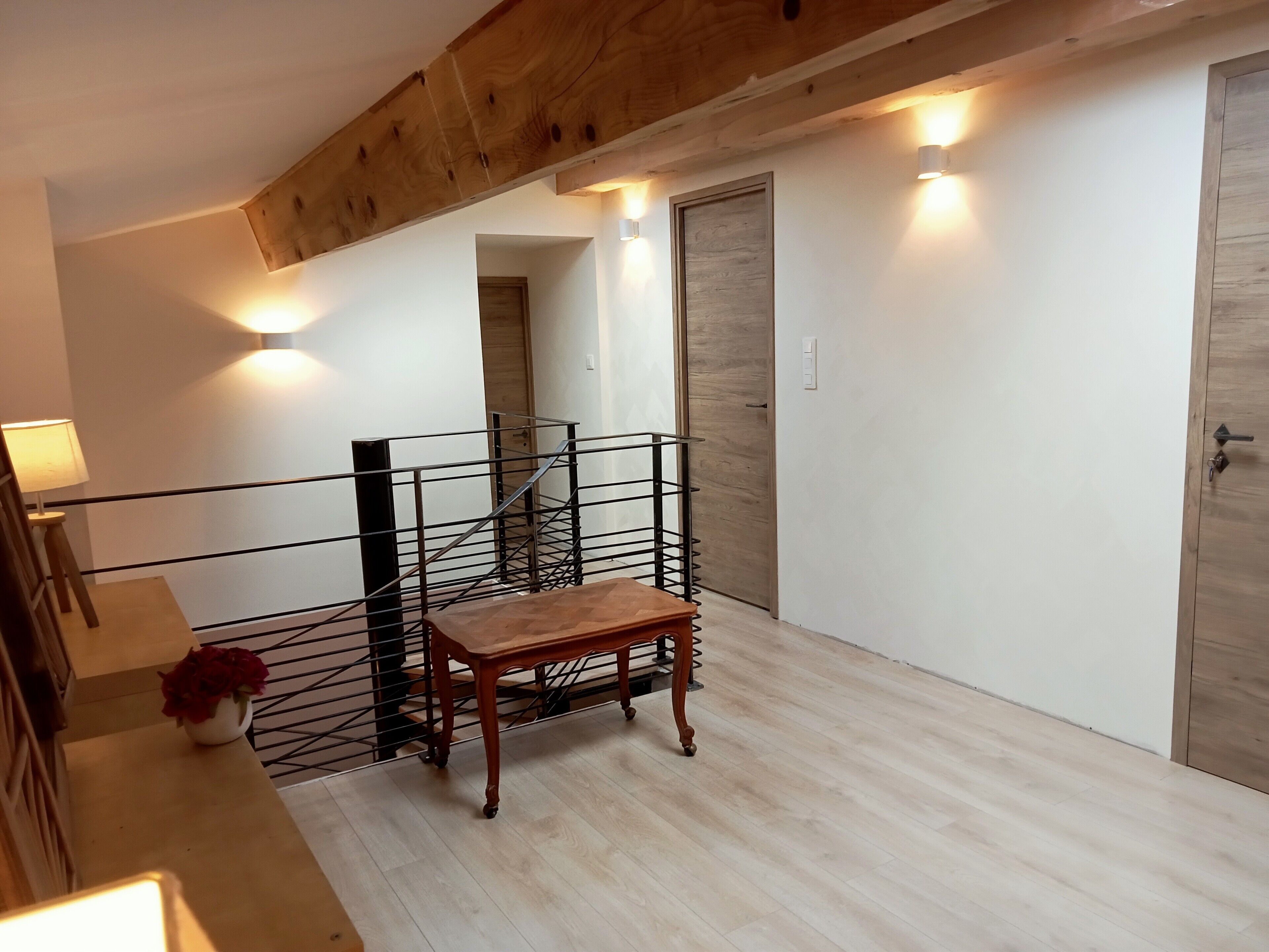 A staircase with a metal railing, a wooden table with a vase of flowers, and a wooden door in a room with white walls and wooden flooring.
