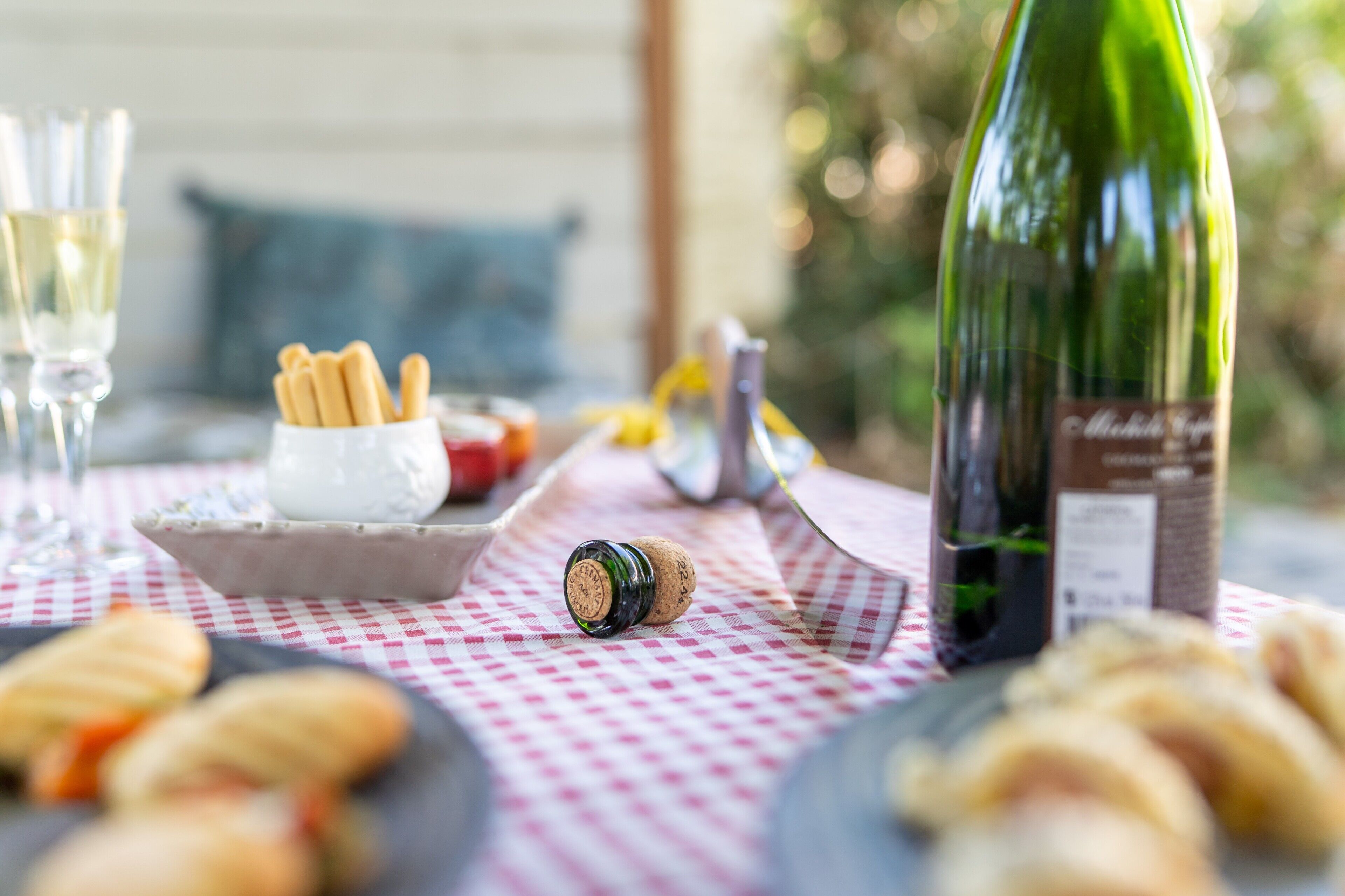 Una mesa con mantel a cuadros, una botella de vino, un sacacorchos y diversas viandas.