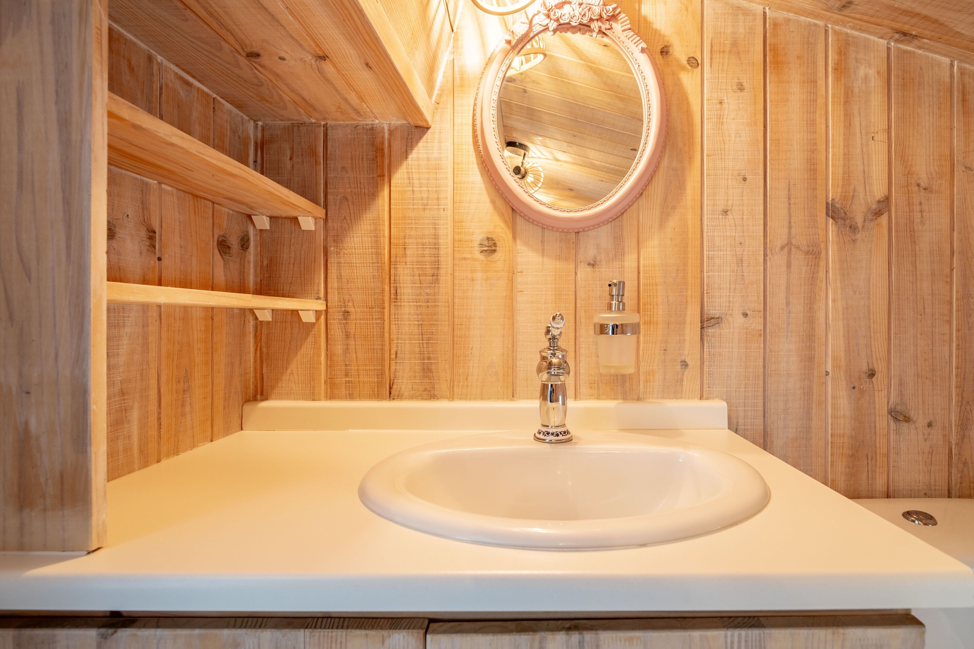 Un interior de madera con un lavabo blanco, un espejo y una repisa.