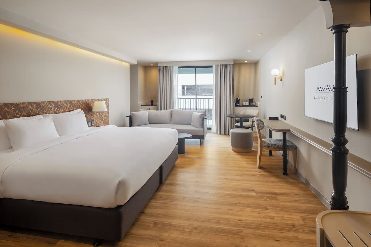 Habitación de hotel con una cama grande, un sofá, una mesa de comedor y un televisor montado en la pared.