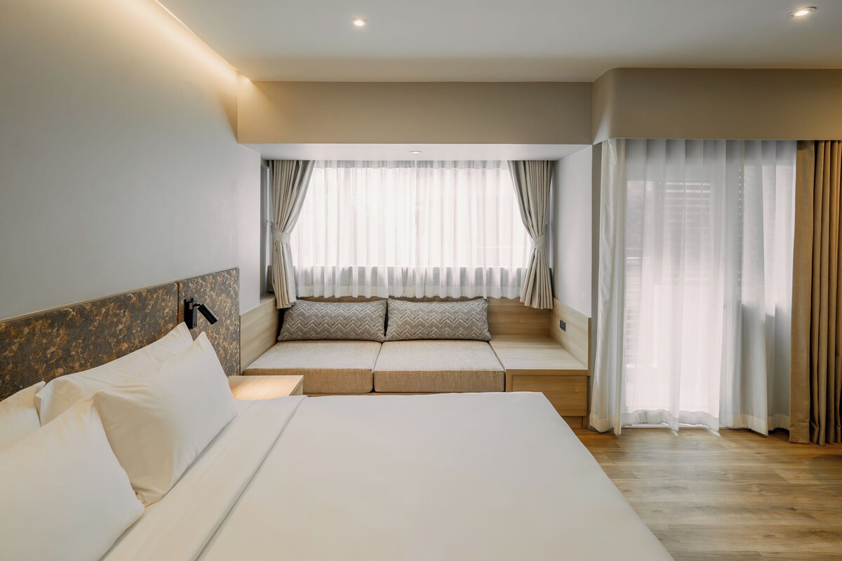 Een hotelkamer met een groot bed, een slaapbank en een raam met dunne gordijnen.