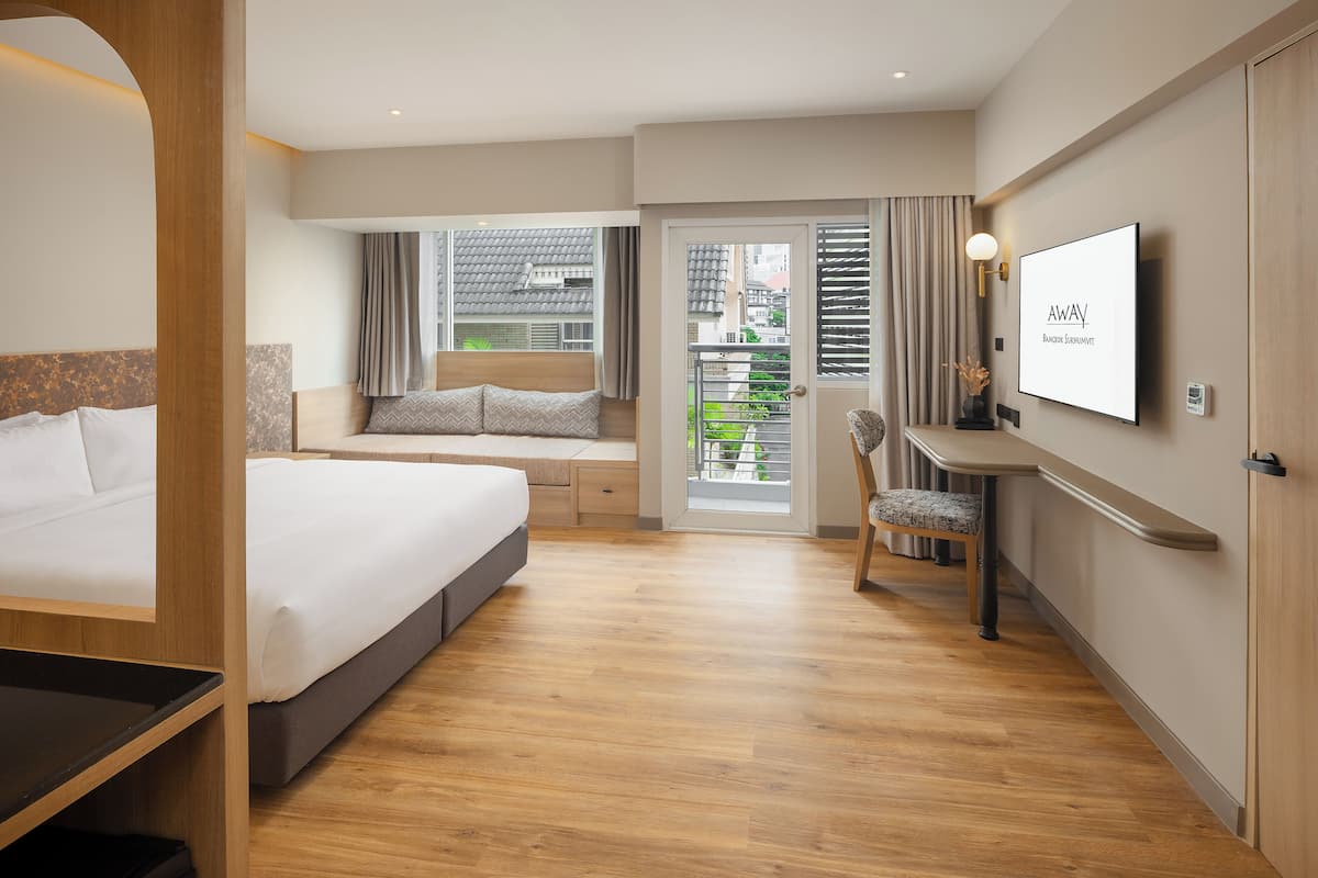 Una habitación de hotel moderna con cama, escritorio, silla, televisor y balcón con vistas a la ciudad.