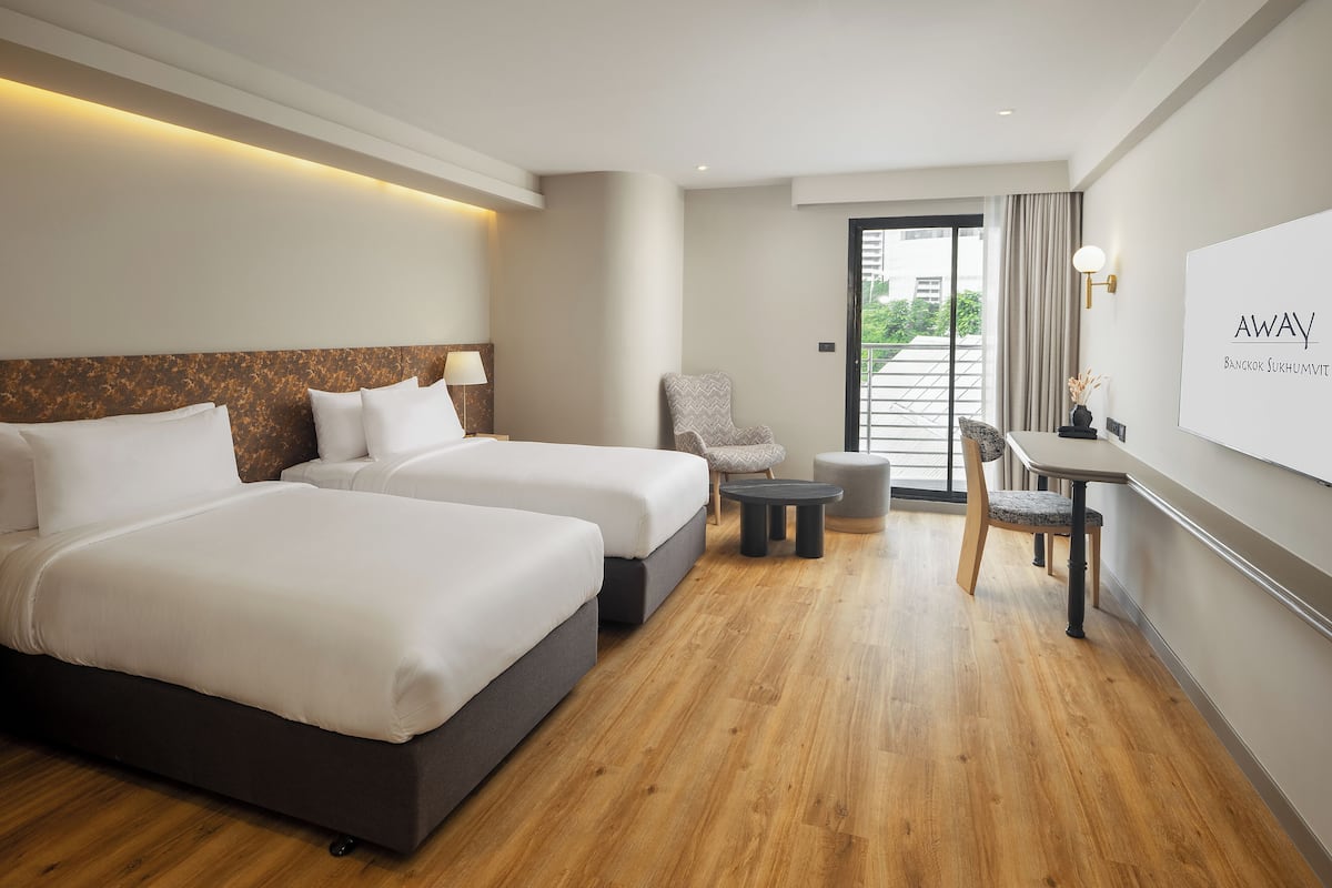 Habitación de hotel con dos camas, una silla, una mesita y vistas al exterior.