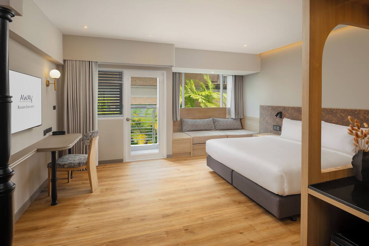 Une chambre d’hôtel moderne avec un lit, un bureau et un coin salon près d’une grande fenêtre.