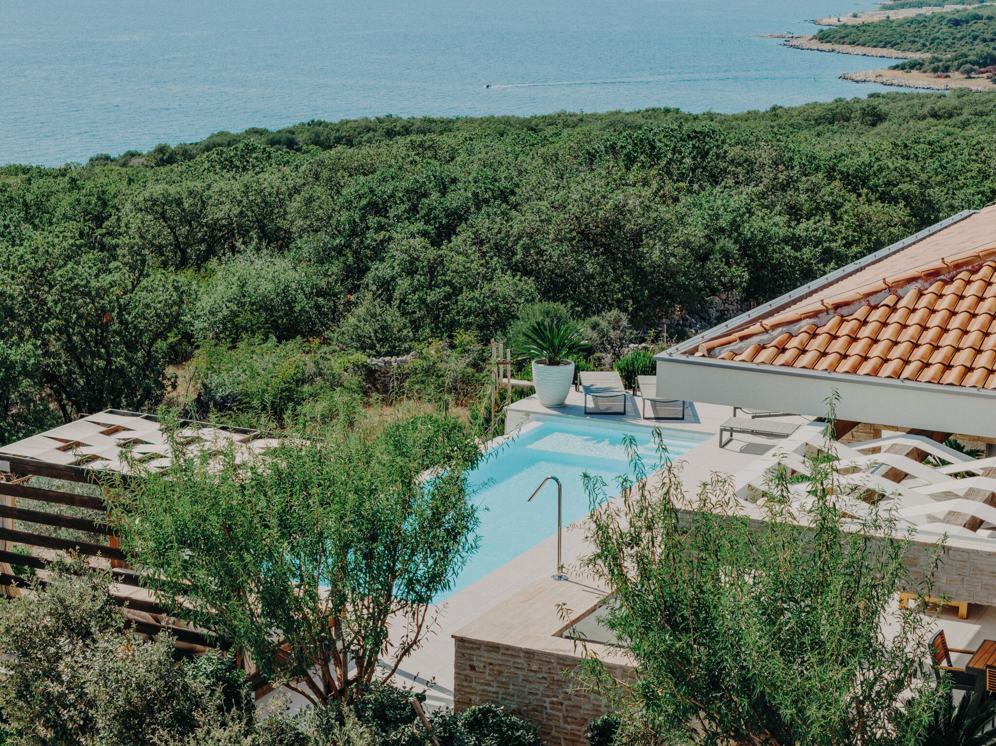 Ein Poolbereich mit Blick auf das Meer, umgeben von Grünpflanzen und Steingebäuden.
