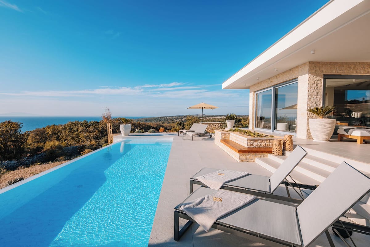 A modern outdoor pool area with lounge chairs and a view of the sea.