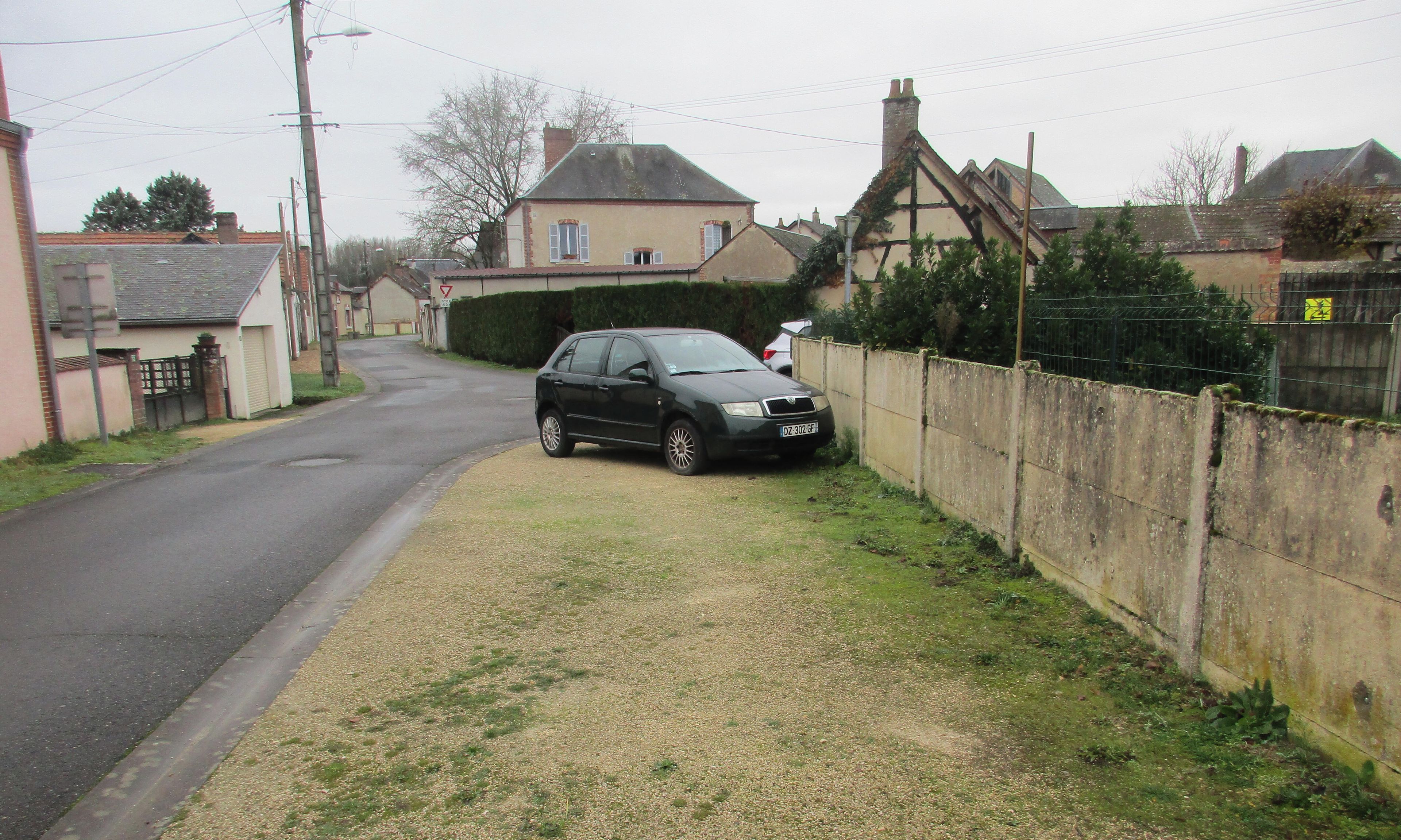 Une rue résidentielle bordée de maisons, avec une voiture garée sur le côté et un espace verdoyant.