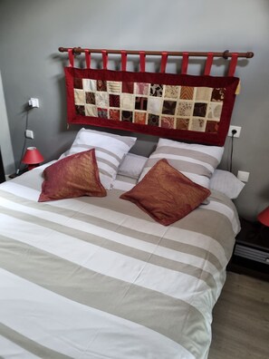 A bed with striped bedding, two red pillows, and a quilted headboard. - Continued from Solognote (Neuvy-sur-Barangeon)