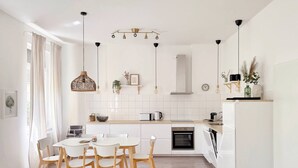 Une cuisine moderne avec des meubles blancs, une table à manger avec des chaises et des luminaires suspendus.