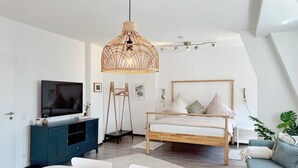 A modern bedroom with a wooden bed, a television, a dining table, and a hanging light fixture.