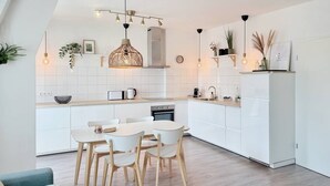A modern kitchen with white cabinets, a dining table with chairs, and pendant lighting.