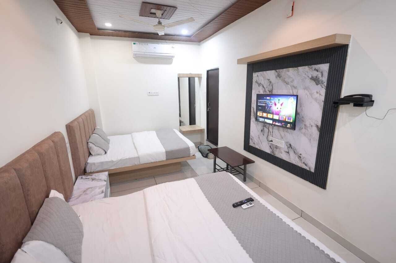 A bedroom with two beds, a TV mounted on the wall, a ceiling fan, and a small table.