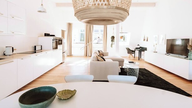 A modern kitchen with white cabinets, a dining area with a white table, and a living room with a white sofa. - 06 Deichstadt-Apartments Neuwied  104m² (Neuwied)