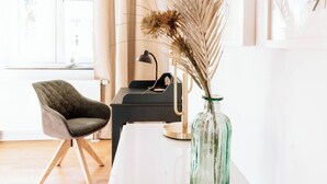 A modern room with a wooden floor, a desk with a lamp, a chair, and a vase with dried plants. - 06 Deichstadt-Apartments Neuwied  104m² (Neuwied)