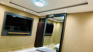 A modern hotel room with a large bed, a flat-screen TV mounted on the wall, a ceiling light, and a mirror.