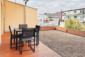 A balcony with a wooden table and chairs, a hanging chair, and a view of the cityscape. - 07 Deichstadt-Apartments Neuwied   116m² (Neuwied)