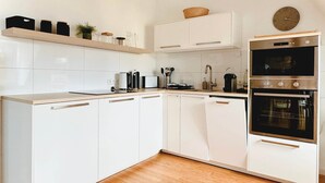 A modern kitchen with white cabinetry, a wooden countertop, a built-in oven, and a clock on the wall.