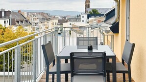 A balcony with a table and chairs, overlooking a town with a church spire in the distance.