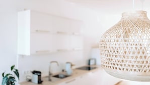 A modern kitchen with white cabinets, a hanging woven light fixture, and a coffee maker on the counter.