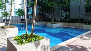 A swimming pool surrounded by planters with tropical plants, set against a modern building facade.