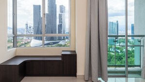 A modern room with a large window offering a city view, a dark wood bench, and a balcony with a glass railing.