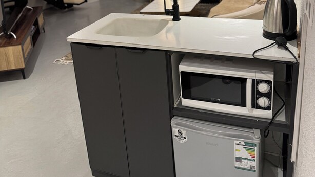Une cuisine compacte équipée d’un four à micro-ondes encastré, d’un petit réfrigérateur et d’un évier.