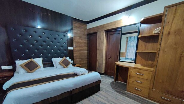 A bedroom with a large bed, wooden wardrobe, and a mirror. - Mountain Retreat (Leh)