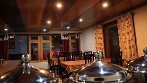 A restaurant with wooden ceiling beams, tables with tablecloths, and curtains. - Mountain Retreat (Leh)