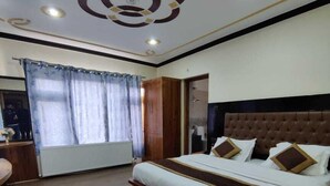 A bedroom with a large bed, wooden flooring, a wardrobe, and a bathroom visible through an open door. - Mountain Retreat (Leh)