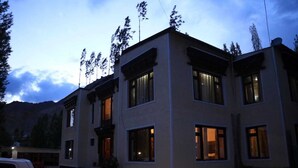 A two-story building with large windows and a balcony, surrounded by mountains. - Mountain Retreat (Leh)