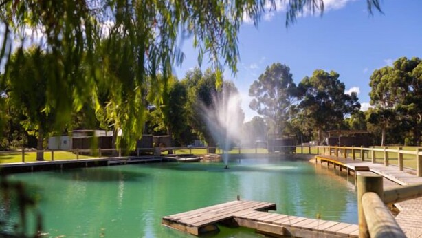 Una piscina amb una terrassa de fusta, envoltada d'arbres i un cel clar.