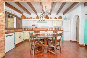 Una cocina con armarios de madera, una mesa de comedor con sillas, una lámpara colgante y una ventana con barrotes.