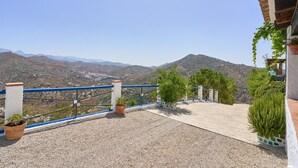 A terrace with a view of mountains, a blue railing, and potted plants.