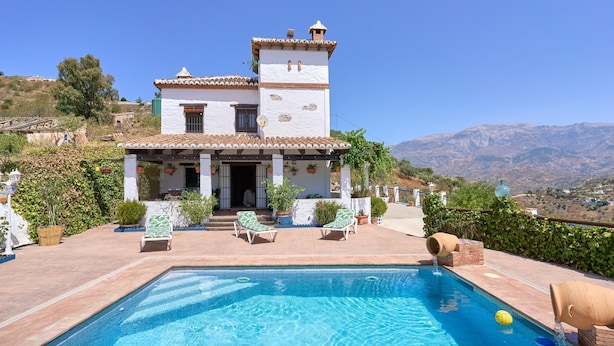 A pool area with a clear view of the pool, lounge chairs, and a building with a tiled roof.