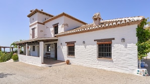 A two-story white building with a tiled roof, a covered patio, and a gravel driveway.