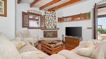 Un salon chaleureux avec une cheminée en pierre, des poutres apparentes, un téléviseur et des fauteuils confortables.