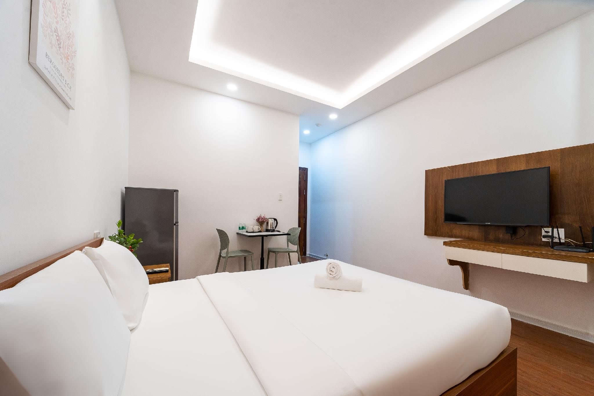 Habitación de hotel con cama, un escritorio con silla, televisor montado en un panel de madera y una lámpara en el techo.