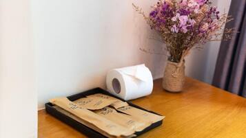 A wooden table with a roll of toilet paper, a vase with dried flowers, and a tray with paper bags.