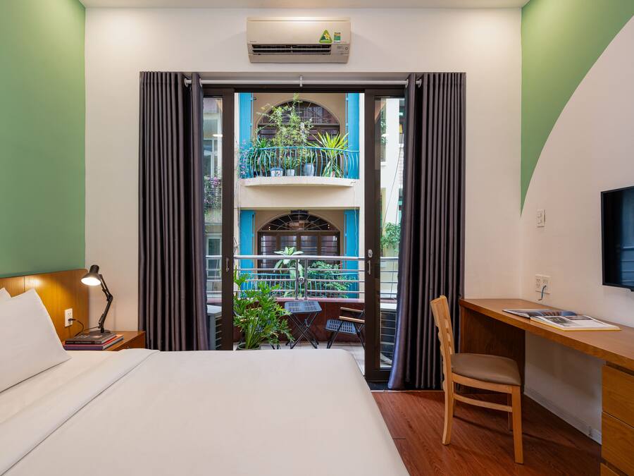 Una camera d'albergo con un letto, una scrivania, una sedia e un balcone con piante.