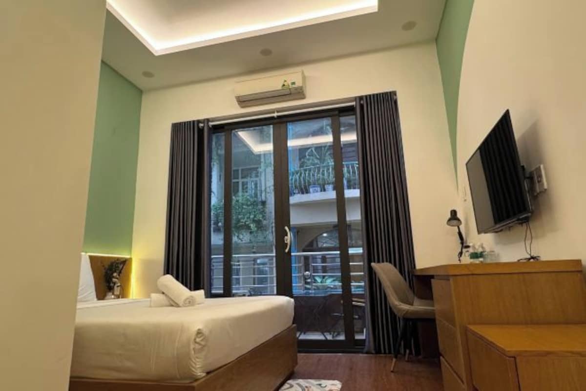 A hotel room with a bed, a desk, a chair, a TV, and a balcony with a view of the outside.