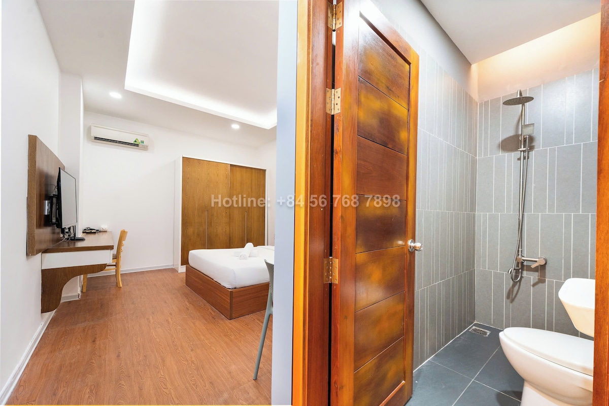 A hotel room with a wooden desk, a bed, a shower, and a toilet.